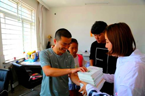 图为女孩班主任陆老师（右一）接过刘春（左一）捐赠的书籍